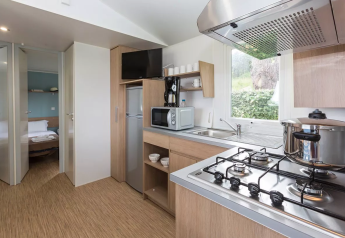 Cucina glamping moderna con fornello a gas, pentola, frigo, microonde e vista sulla camera e la natura.