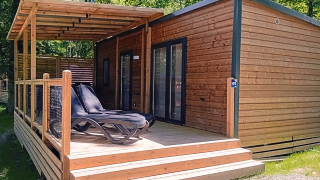 Houten lodge met overdekt terras en ligstoelen in een groene omgeving, Homeflower Premium lodge.