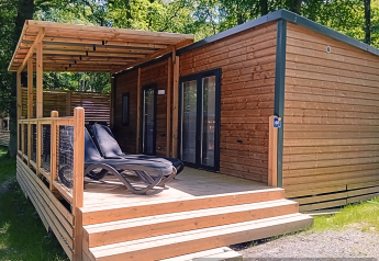 Trælodge med overdækket terrasse og liggestole i et grønt, skovområde, Homeflower Premium lodge.