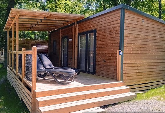 Houten lodge met overdekt terras en ligstoelen in een groene omgeving, Homeflower Premium lodge.