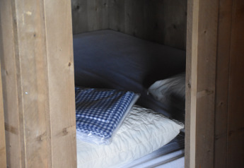 A cozy wooden cabin bedroom at Kidz Lodge, Duynpark Het Zwanenwater, Netherlands, with bed, pillow, and blanket.