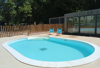 Udendørs swimmingpool med to blå liggestole ved Camping Seasonova Vittel i Grand Est, Frankrig, omgivet af træer.