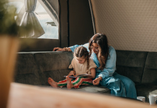 Mama en dochter lezen samen in de Big Oak Tent bij Holiday Park Sallandshoeve, Nederland.