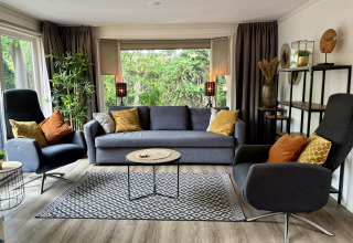 Moderne woonkamer in Cozy Lodge bij Bungalowpark Het Verscholen Dorp, Nederland, met zetels en grote ramen.