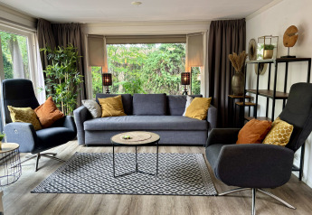 Moderne stue i Cozy Lodge ved Bungalowpark Het Verscholen Dorp, Holland, med sofa, lænestole og store vinduer.