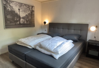 Soveværelse på Cozy Lodge i Bungalowpark Het Verscholen Dorp med dobbeltseng, sort-hvid vægbillede og natborde.