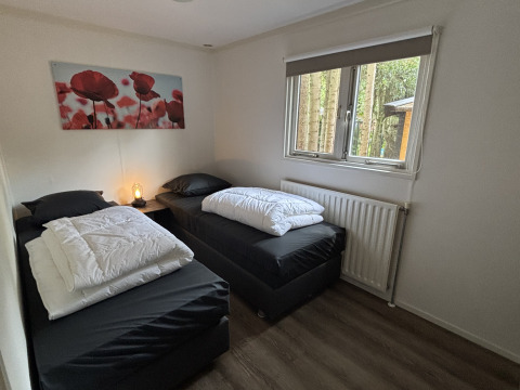 Twee eenpersoonsbedden met zwart beddengoed in een kamer van Cozy Lodge, Bungalowpark Het Verscholen Dorp.