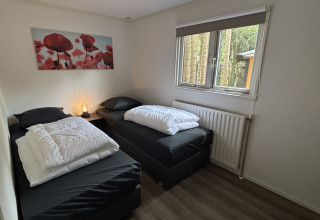 Twee eenpersoonsbedden met zwart beddengoed in een kamer van Cozy Lodge, Bungalowpark Het Verscholen Dorp.
