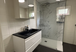 Moderne badkamer met zwarte wastafel, spiegelkast en douche in Cozy Lodge, Bungalowpark Het Verscholen Dorp.