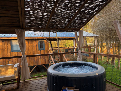 Terraza exterior con jacuzzi burbujeante y asientos en Charme hut met jacuzzi, Camping Le Périgord, Francia.