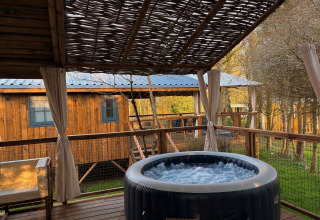 Terraza exterior con jacuzzi burbujeante y asientos en Charme hut met jacuzzi, Camping Le Périgord, Francia.