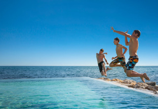 Tre ragazzi saltano in piscina vicino al mare ad Aminess Planet Camping Sirena in Istria, Croazia.