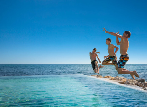 Tre drenge hopper i swimmingpoolen ved Aminess Planet Camping Sirena ved havet i Istrien, Kroatien.