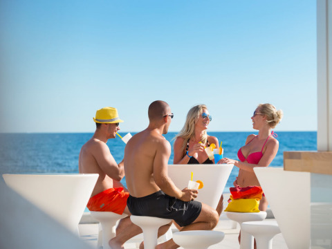Vier vrienden drinken samen aan een witte tafel bij Aminess Planet Camping Sirena met uitzicht op zee in Istrië.