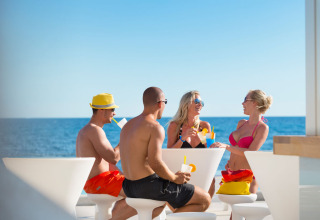 Vier vrienden drinken samen aan een witte tafel met zeezicht bij Aminess Planet Camping Sirena in Istrië, Kroatië.