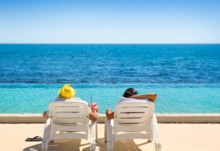 Due persone si rilassano su lettini a bordo piscina con vista sul mare ad Aminess Planet Camping Sirena, Istria.