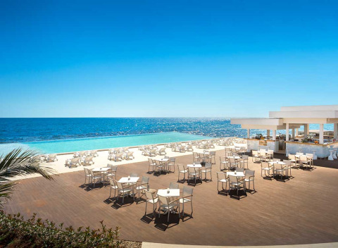 Zona pranzo esterna ad Aminess Planet Camping Sirena con tavoli bianchi, piscina infinity e vista mare.