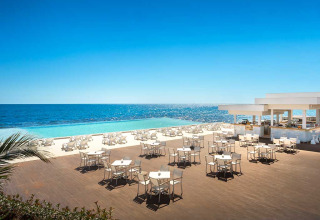 Outdoor dining area at Aminess Planet Camping Sirena, featuring white tables, infinity pool, and sea view.