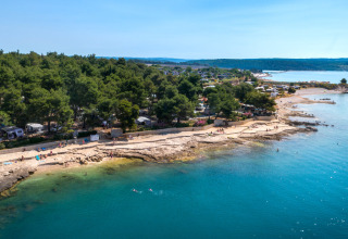 Kustcamping en rotsachtige strand bij Novigrad, Istrië, Kroatië, met helderblauw water en veel bomen.