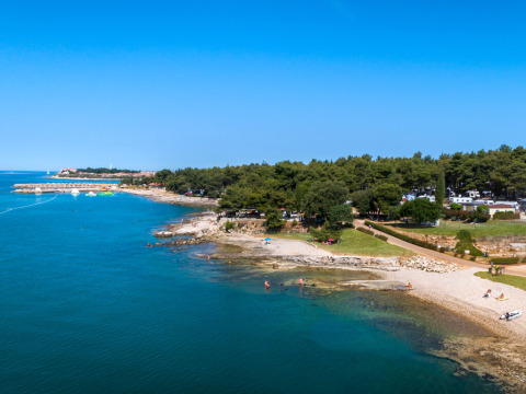 Kystlinje ved Aminess Planet Camping Sirena i Istrien, Kroatien med blåt hav, strand og grønne træer.