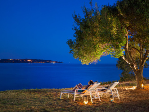 Due persone rilassate su lettini sotto un albero presso il mare la sera ad Aminess Planet Camping Sirena, Istria.