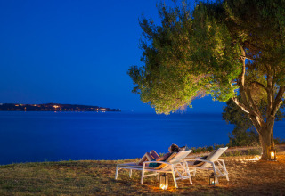 Dos personas descansan en tumbonas bajo un árbol junto al mar al atardecer en Aminess Planet Camping Sirena, Istria.