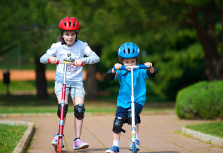 Two kids wearing helmets and knee pads ride scooters on a path at Aminess Planet Camping Sirena, Istria, Croatia.