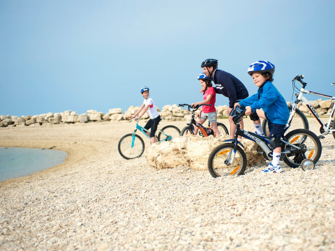 Gezin met helmen fietst op het kiezelstrand bij Aminess Planet Camping Sirena in Istrië, Kroatië.