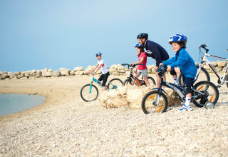 Famiglia con caschi che va in bici insieme sulla spiaggia di sassi ad Aminess Planet Camping Sirena, Istria.