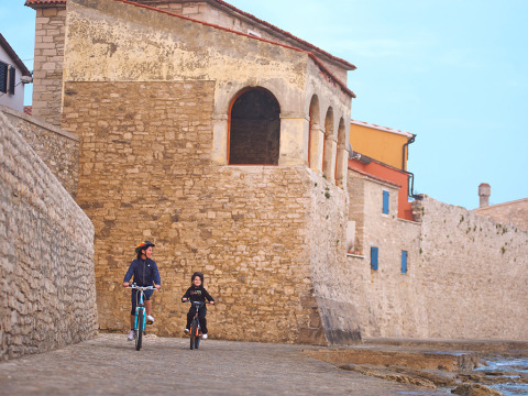 Due persone vanno in bicicletta lungo un antico muro di pietra a Novigrad, in Istria, Croazia.