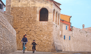 Zwei Menschen fahren Fahrrad entlang einer alten Steinmauer in der Nähe von Novigrad, Istrien, Kroatien.
