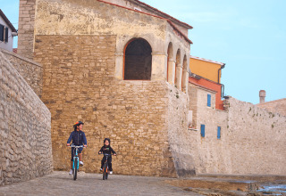 Twee mensen fietsen langs een oude stenen muur in Novigrad, Istrië, Kroatië op een heldere dag.