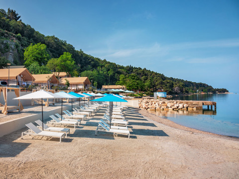 Solrige strandstole og parasoller ved Valamar Camping Lanterna i Istrien, Kroatien, nær det klare blå hav.