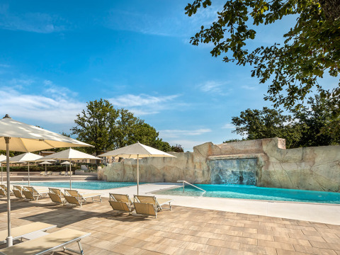 Zona de piscina exterior con tumbonas, sombrillas y cascada en Valamar Camping Lanterna, Istria, Croacia.