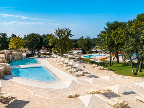 Outdoor swimming pool and sun loungers with umbrellas at Valamar Camping Lanterna holiday park in Istria, Croatia.