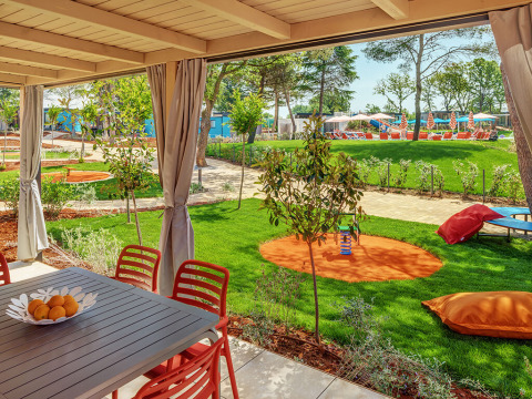 Blick aus dem Maro Home Chalet im Valamar Camping Lanterna, mit Terrasse, Gartentisch und Spielbereich.