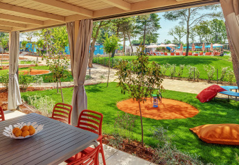 Udsigt fra Maro Home chalet på Valamar Camping Lanterna, med terrasse, grøn græsplæne og legeredskaber.