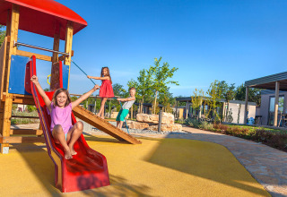 Drie kinderen spelen op een glijbaan bij de speeltuin voor de Maro Home chalets met een heldere blauwe lucht.