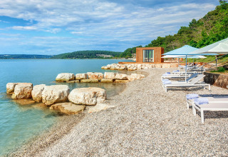 Kiezelstrand met ligbedden, parasols en een luxe safaritentgebouw aan de rustige zee.