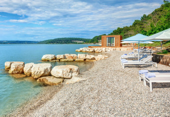 Steinstrand mit Liegestühlen, Sonnenschirmen und einem luxuriösen Safarizeltgebäude am Meer.