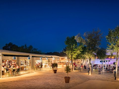 Scena serale al Valamar Camping Lanterna con negozi illuminati, bar e ospiti in Istria, Croazia.