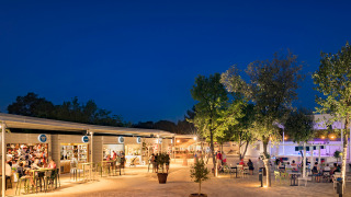 Scena serale al Valamar Camping Lanterna con negozi illuminati, bar e ospiti in Istria, Croazia.