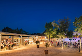 Vista nocturna de Valamar Camping Lanterna con tiendas iluminadas, cafeterías y huéspedes en Istria, Croacia.