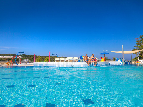 Family relaxes at the waterpark pool under clear skies at Valamar Camping Lanterna, Istria, Croatia holiday park.