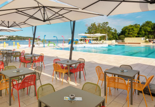 Cafetería al aire libre con sillas y mesas de colores junto a la piscina y vista al mar en Valamar Camping Lanterna, Croacia.