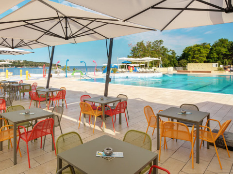 Buitencafé met gekleurde stoelen en tafels bij het zwembad met zeezicht op Valamar Camping Lanterna, Kroatië.