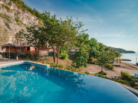 Vista de piscina infinita con tiendas safari, árboles y costa en Valamar Camping Lanterna, Croacia.