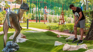Ein Mann spielt Minigolf am Valamar Camping Lanterna in Istrien, Kroatien, neben einer Dino-Statue.