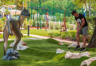 Uomo gioca a minigolf al Valamar Camping Lanterna in Istria, Croazia, accanto a una statua di dinosauro.
