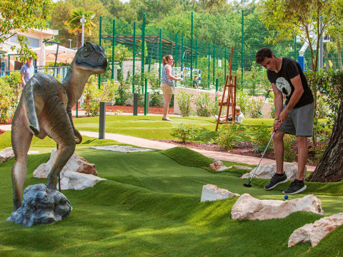 Uomo gioca a minigolf al Valamar Camping Lanterna in Istria, Croazia, accanto a una statua di dinosauro.